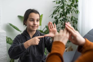 Küçük beyaz kız çocuğu evde şefkatli anne ya da öğretmenle eklem egzersizi yapıyor. Sesleri telaffuz eden küçük bir çocuk hoca ya da koçla konuşur, birlikte sesli telaffuz eder..