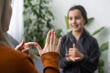 Küçük beyaz kız çocuğu evde şefkatli anne ya da öğretmenle eklem egzersizi yapıyor. Sesleri telaffuz eden küçük bir çocuk hoca ya da koçla konuşur, birlikte sesli telaffuz eder..