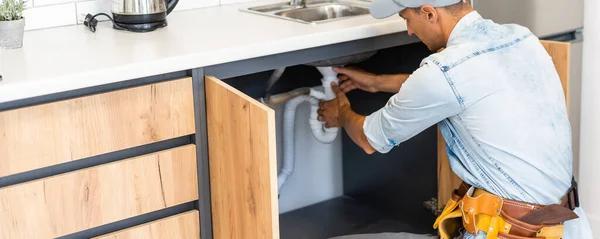 plumber fixes sink siphon by two pipe-wrenches in kitchen