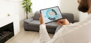 Tablette akıllı ev kontrolü. Arka planda oturma odasının içi..