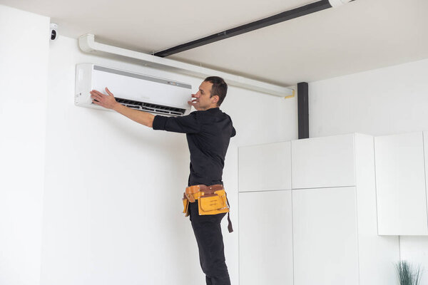 Техник мужского пола устанавливает кондиционер в помещении
.