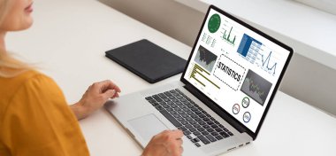 Onun masasında kadın analisti istatistikleri, grafikler ve gösterilen bir dizüstü bilgisayarda çalışır. O yaratıcı ofiste ahşap tabloda çalışıyor. Omuz görüntüleri.