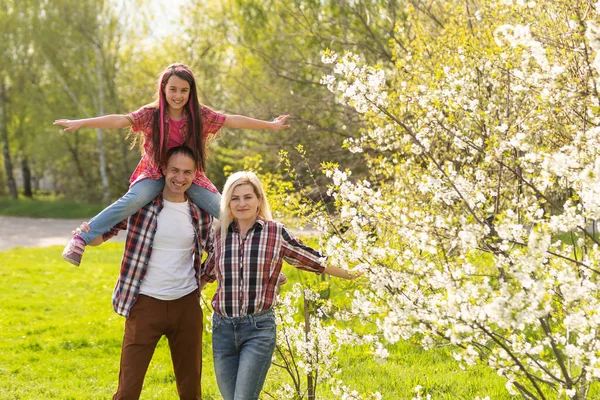 Happy parents mom and dad, daughter, young family outdoors in spring against the background of blooming apple and cherry trees.