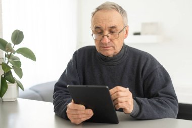 Senior man using tablet computer at home in the living room