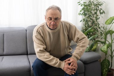 old man with his knee joint pain in sofa, pain in the elderly, health care, elderly care. Elderly man having a knee pain and sitting down. Grandfather with knee pain