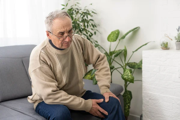 old man with his knee joint pain in sofa, pain in the elderly, health care, elderly care. Elderly man having a knee pain and sitting down. Grandfather with knee pain
