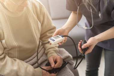 Smiling young nurse taking old mans blood pressure.