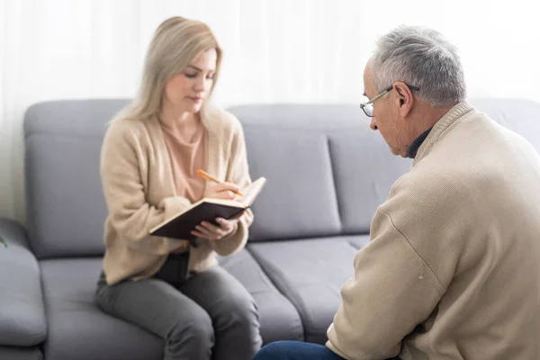 Mature man at a session with a psychologist. The doctor listens and writes. Help with depression, psychiatric diagnosis