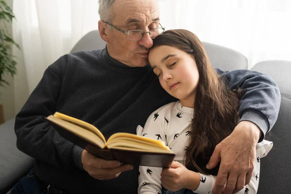 Book, family and children with a girl reading to her grandfather on the floor of their living at home. Kids, read and story with a senior man and granddaughter bonding in their house during a visit