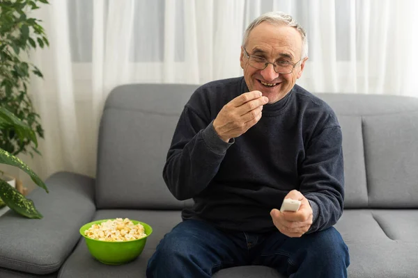 Portrait of elderly man watching TV with popcorn and a remote control.