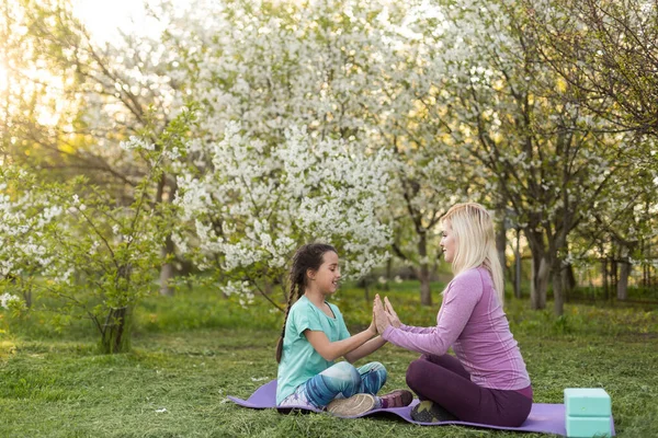 Family Mother teacher training yoga child daughter on a yoga mat at home garden. Family outdoors. Parent with child spends time together. exercise at home concept and new normal
