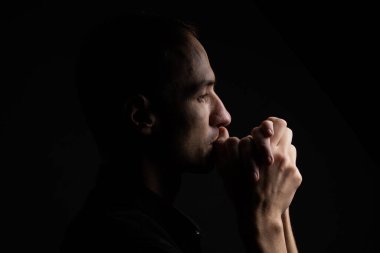 Elleri sıkıca bağlı siyah arka planda dua eden adam..