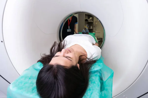 CT scan technologist overlooking patient in Computed Tomography scanner during preparation for procedure. Woman patient going into CT scanner