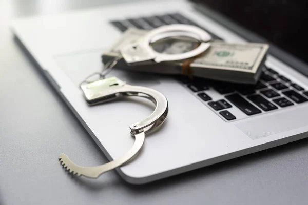 Cyber crime legal law police handcuffs on a hundred dollar bills with computer keyboard technology of criminal taking fingerprint on paper.