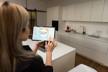 Iot Smart Home Concept - rear view of woman ask digital tablet to set temperature of air conditioner more higher by voice at home and all the electric meter in house getting energy-efficient.