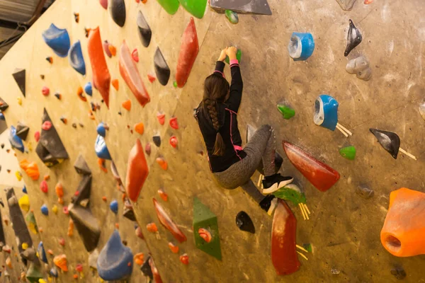 Girl climbing on practical wall indoor, bouldering training.