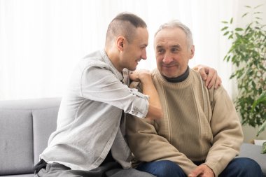 Help needed. Pleasant senior man sitting on the sofa.