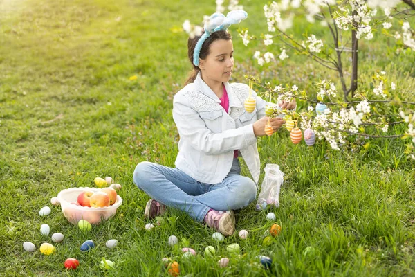 ウサギの耳の中で愛らしい女の子は 春の日に屋外で木の枝を咲かせます 庭でイースターエッグハントを楽しんでいる子供 — ストック写真
