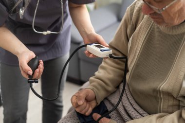 Hemşire, klinikteki yaşlı hasta bir erkek hastanın yüksek tansiyonunu ölçüyor. Doktor hipertansiyonu olan yaşlı bir adamın kan basıncını ölçüyor. Sağlık hizmetleri kavramı.