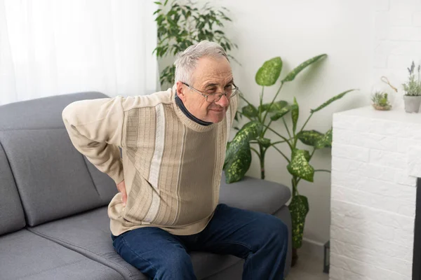 Caucasian old senior elderly unhealthy sickness grey male grandpa near sofa at home alone holding hands on back having emergency painful muscle and backache injury problem
