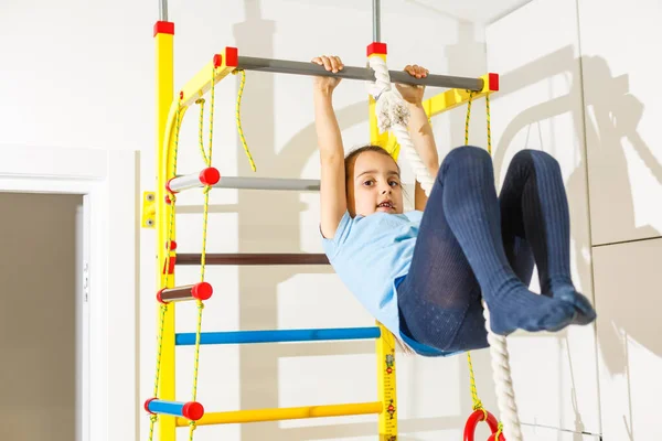 Portrait of a happy child in a gaming entertainment center. The sweating little girl hanging on a soft horizontal bar. A beautiful active baby goes in for sports.