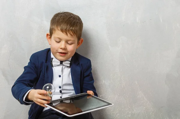 Vrolijke Kleine Jongen Met Digitale Tablet Tegen Een Grijze Achtergrond — Stockfoto