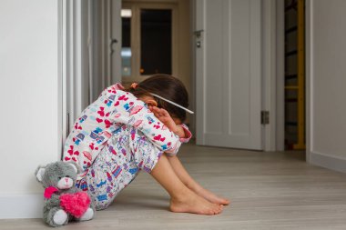 Koridorun zemininde oturan genç bir ilkokul öğrencisi koridorda ağlıyor. Çocukluk konsepti. Gerçek insanlar. Boşluğu kopyala.