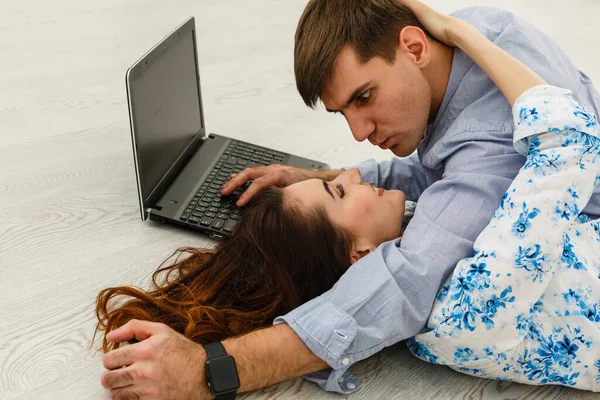 Couple Use Laptop Computer, while Sitting on the Living Floor room of their Apartment. Boyfriend and Girlfriend Talk, Shop on Internet, Choose Product to Order Online, Watch Streaming Service