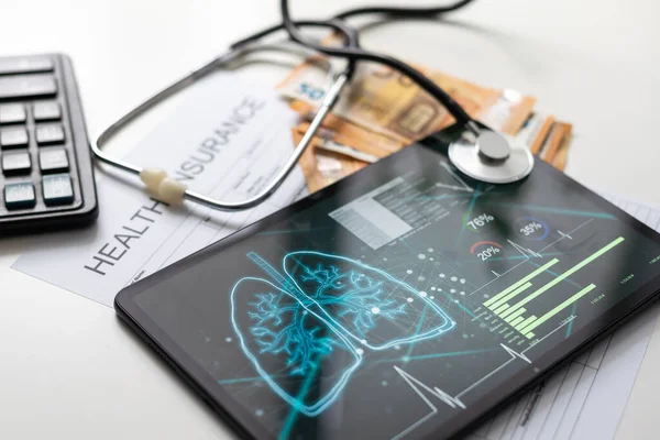 Modern social health insurance program. Tablet computer with healthcare application interface on screen. Stethoscope, x-ray image and cardiogram on wooden desk. Digital healthcare technologies.