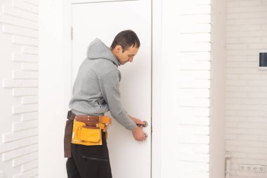Young handyman installing a white door in a room.