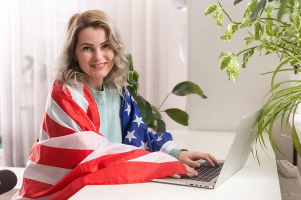 stock image Happy woman employee sitting wrapped in USA flag, shouting for joy in office workplace, celebrating labor day or US Independence day