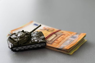 Ahşap arka planda bir yığın avro banknotunda plastik oyuncak tankları.