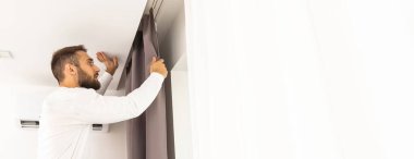 Genç adam perdeler pencere üzerinde yükleme.