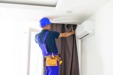 Genç yakışıklı bir adam ya da tamirci evdeki perdeleri takıyor, tadilat yapıyor.