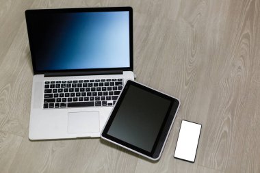 Modern dizüstü bilgisayar, cep telefonu, tablet ve beyaz ahşap arka plan üzerine not defteri.