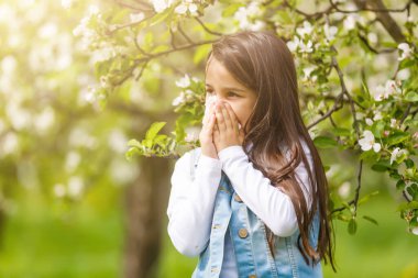 Little girl is blowing her nose while on green meadow clipart