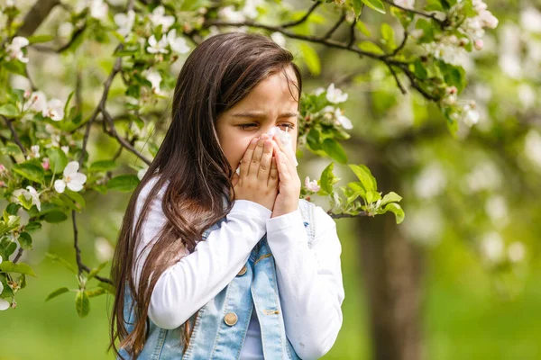 stock image Little girl is blowing her nose near spring tree in bloom