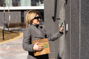 Akıllı ev kavramı - Kutu telefonu olan kadına yakın çekim yapmak için elektronik kilit açmak için cep telefonu kullanın.