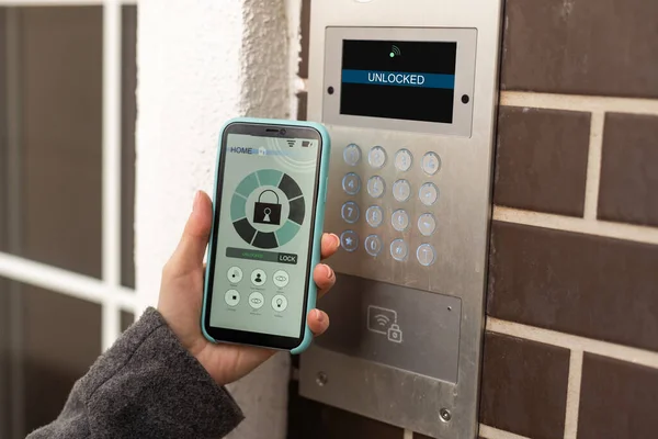 Young stylish woman getting access to the building by attaching smartphone to intercom. Concept of modern security technologies for access and smart home.