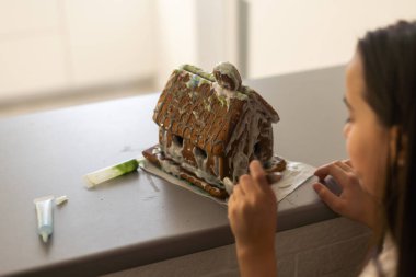 Bir kız geleneksel Noel süsü olarak zencefilli kurabiye eviyle oynuyor..