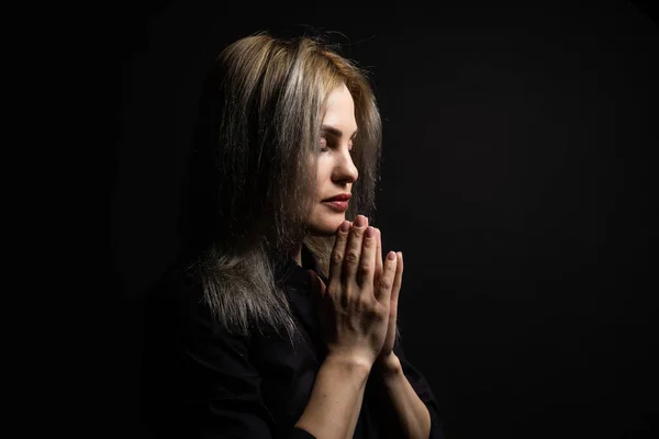 Woman praying with hands together on black background.
