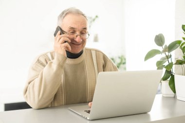 Handsome mature man in casual sitting in home office and working at laptop.