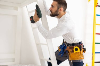 A man with instructions for assembling furniture is going to assemble in a childrens bedroom.