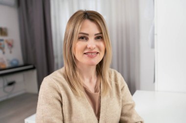 Güzel, neşeli bir kadın, sarışın, sıradan giyinmiş, kameraya tatmin edici bir şekilde bakıyor, mutlu. Güzel bir kadının stüdyo resmi. Boş bir stüdyo duvarında izole edilmiş..