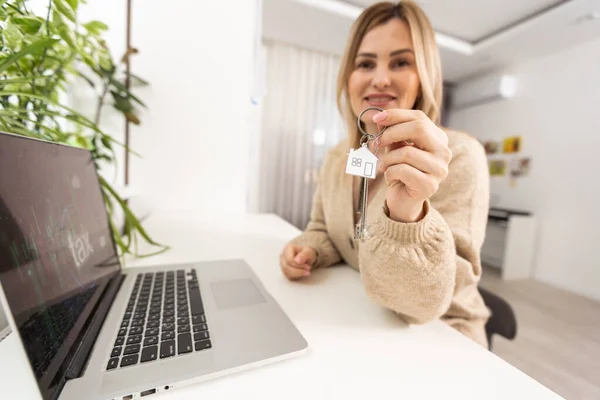 Woman holding keys with laptop and taxes.