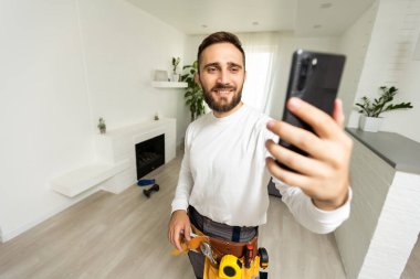 Gülümseyen yakışıklı inşaatçı cep telefonuyla selfie çekiyor..
