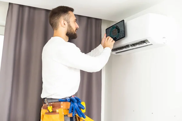 家の中でデジタルタブレットやペンチェックエアコンを使用して若い技術者 空調システムの設置と修理のコンセプト — ストック写真