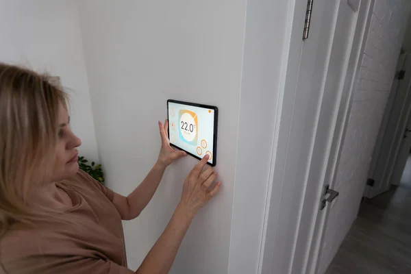 Controlling home with a digital touch screen panel installed on the wall in the living room. Concept of a smart home and mobile application for managing smart devices at home.