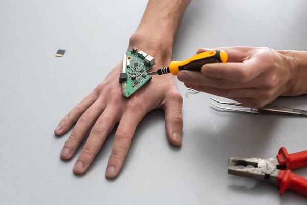 Robot arm concept. Man shows biomechanical prosthetic hand. Guy repairs his hand with tool. Bioengineering, transhumanism, biohacking, human cyborg. Fusion of electronics, mechanics and the human body