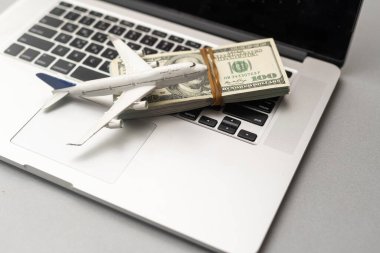 Cash in american dollar banknotes with plastic airplane model and laptop computer keyboard